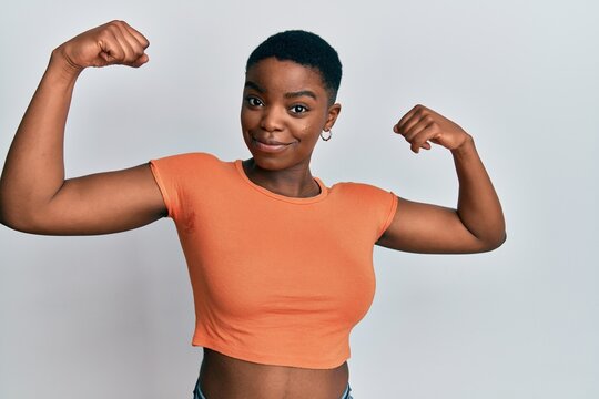 Young african american woman wearing casual orange t shirt showing arms muscles smiling proud. fitness concept.