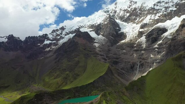 Wide rising drone shot in the Andes mountains, with snow covered mountains and a turquoise colored glacial lake