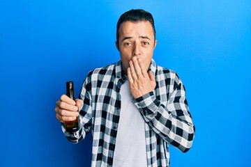 Handsome young man drinking a pint of beer covering mouth with hand, shocked and afraid for...
