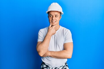 Handsome young man wearing builder uniform and hardhat with hand on chin thinking about question, pensive expression. smiling with thoughtful face. doubt concept.