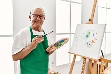 Senior grey-haired artist man smiling happy painting at art studio.