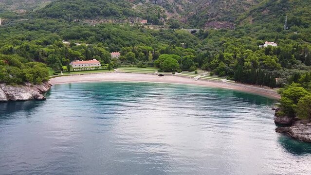 Quiet harbor at the foot of the mountain. Several buildings and empty beach. Drone Shot of King's Beach (Milocer Beach) in Montenegro.