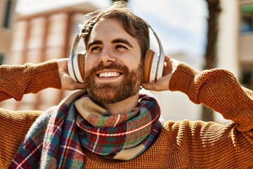 Young caucasian man with beard listening to music wearing headphones outdoors on a sunny day