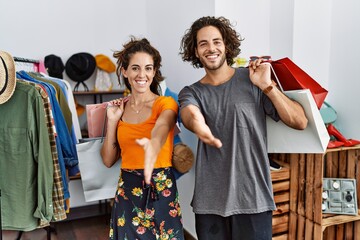 Obraz premium Young hispanic couple holding shopping bags at retail shop smiling friendly offering handshake as greeting and welcoming. successful business.