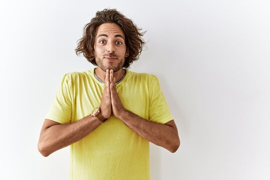 Young hispanic man standing over isolated background praying with hands together asking for forgiveness smiling confident.