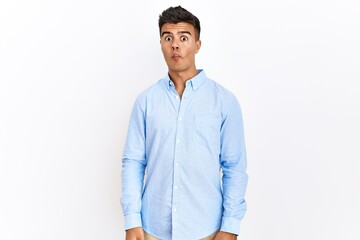 Young hispanic man wearing business shirt standing over isolated background making fish face with lips, crazy and comical gesture. funny expression.