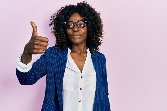 Young african american woman wearing business clothes and glasses looking proud, smiling doing thumbs up gesture to the side