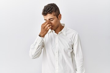 Young handsome hispanic man standing over isolated background tired rubbing nose and eyes feeling fatigue and headache. stress and frustration concept.