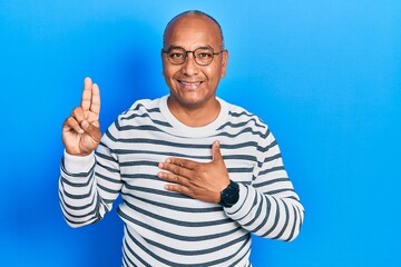 Middle age latin man wearing casual clothes and glasses smiling swearing with hand on chest and...
