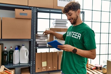 Young arab man wearing volunteer uniform using touchpad at charity center