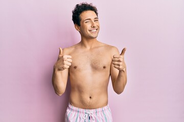 Young handsome man wearing swimwear shirtless success sign doing positive gesture with hand, thumbs up smiling and happy. cheerful expression and winner gesture.