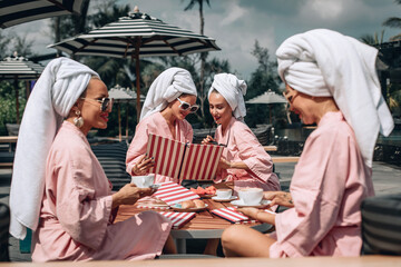 Successful skinny adorable female best friends having fun spending their morning in a summer outdoor cafe looking at the menu and choosing what to order. The same clothes. Leisure lifestyle