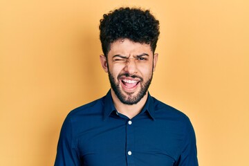 Young arab man with beard wearing casual shirt winking looking at the camera with sexy expression, cheerful and happy face.