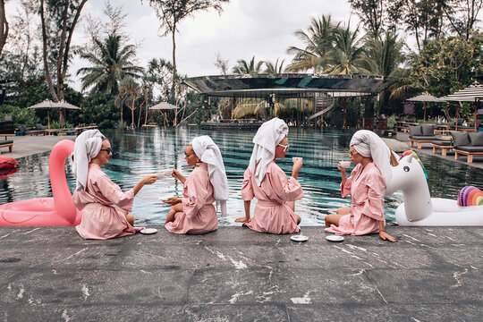 Four girlfriends, divided into pairs, sitting next to the pool and drinking a cup of tea. Girls in the same clothes. Casual concept