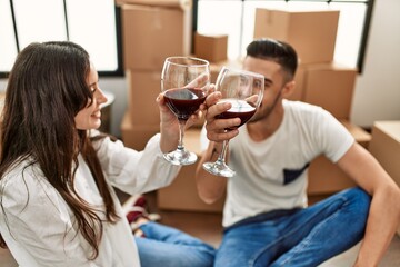 Young hispanic couple smiling happy toasting with red wine at new home.