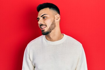 Young hispanic man with beard wearing casual winter sweater looking to side, relax profile pose with natural face and confident smile.