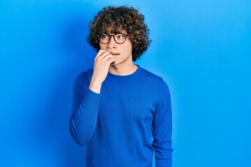 Handsome young man wearing casual clothes and glasses looking stressed and nervous with hands on mouth biting nails. anxiety problem.