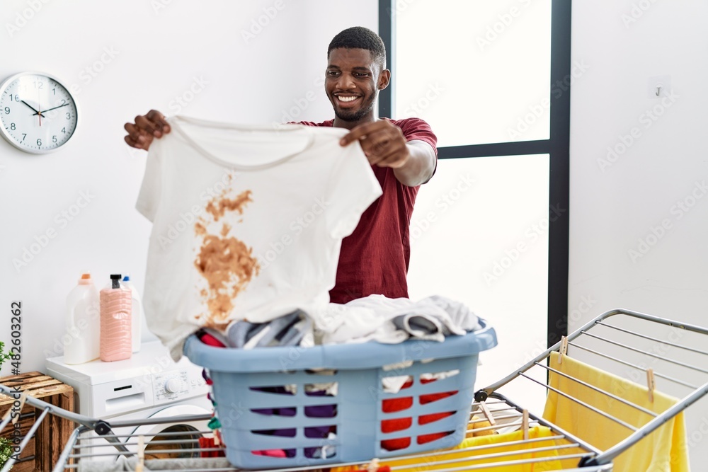 Sticker young african american man smiling confident holding dirty clothes at laundry room