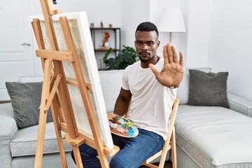 Young african man painting on canvas at home doing stop sing with palm of the hand. warning expression with negative and serious gesture on the face.