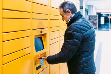 Man in coat scans a code on his mobile phone to pick up a package from the yellow locker. Messaging concept, compare online, e-commerce and packages