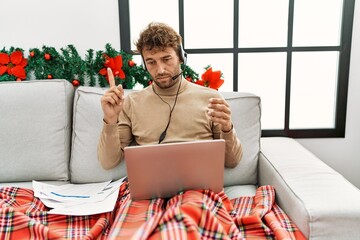 Young hispanic man having video call working sitting by christmas decor at home