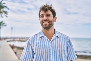 Fototapeta premium Young hispanic man smiling happy standing at the beach.