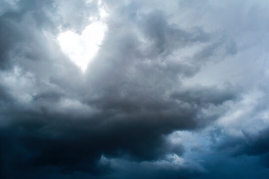 Dramatic stormy sky with bright heart among the dark storm clouds.