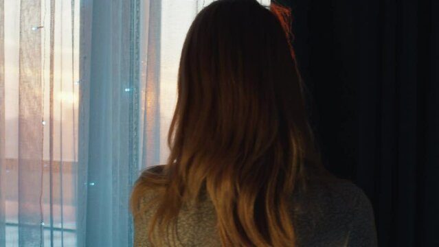 Young woman watches sunset trough the window