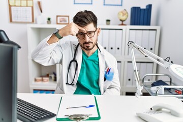 Young man with beard wearing doctor uniform and stethoscope at the clinic pointing unhappy to...