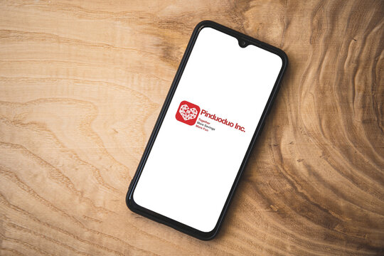 Pinduoduo application on smartphone. Wooden background. Top angle shot