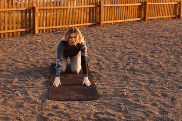 Young blonde woman is stretching on a playground on a yoga mat. Healthy energetic active lifestyle concept.