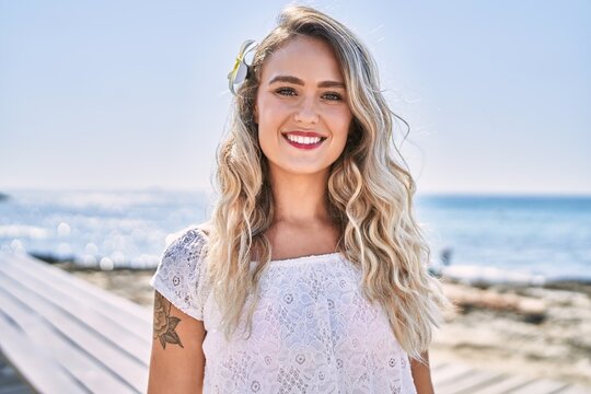 Young blonde girl smiling happy standing at the beach.