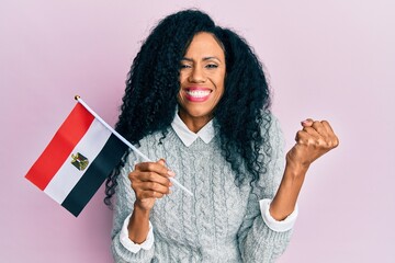 Middle age african american woman holding egypt flag screaming proud, celebrating victory and...