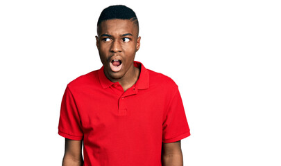Young african american man wearing casual red t shirt angry and mad screaming frustrated and furious, shouting with anger. rage and aggressive concept.