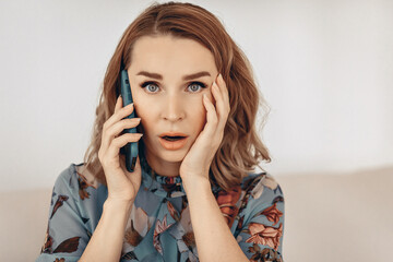 Portrait of a lovely shocked boss lady wearing a blue shirt with a surprised face is talking on the phone and holding on her face. Concept of a dialogue