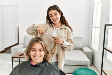Young woman cutting hair to her girlfriend at home.