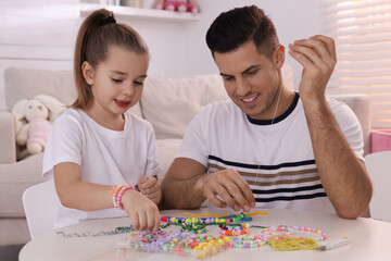 Obraz na płótnie Canvas Happy father with his cute daughter making beaded jewelry at table in room