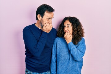 Middle age couple of hispanic woman and man hugging and standing together looking stressed and nervous with hands on mouth biting nails. anxiety problem.