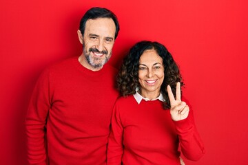 Middle age couple of hispanic woman and man hugging and standing together showing and pointing up with fingers number two while smiling confident and happy.