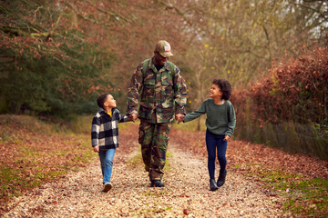 American Soldier In Uniform Returning Home On Leave To Family Holding Hands With Two Children