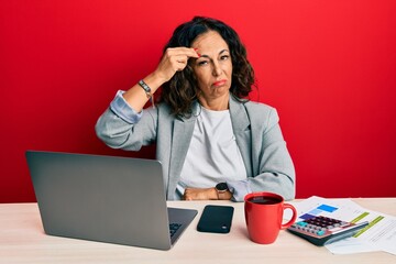 Beautiful middle age woman working at the office drinking a cup of coffee worried and stressed about a problem with hand on forehead, nervous and anxious for crisis