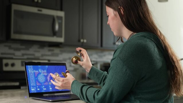 Woman takes remote lesson to learn finger cymbals online on a laptop. Remote learning concept.
