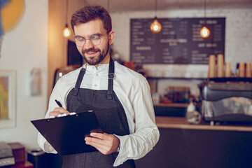 Cheerful male worker writing on clipboard in cafe
