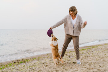 Senior woman smiling while playing with her dog on sandy beach