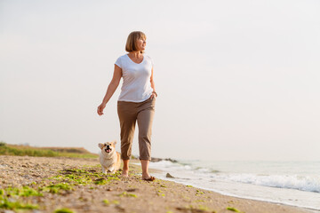 Senior woman smiling while walking her dog on sandy beach