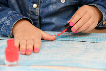 A little girl ineptly paints her nails with varnish from her mother's cosmetics.