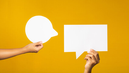 Hand holding of an empty white speech bubble against a yellow background.