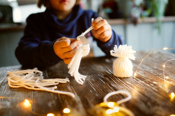 A cute caucasian child at a wooden table makes hats from yarn and sleeves from toilet paper, child...