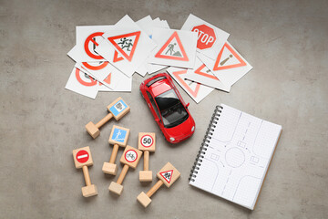 Many different road signs, notebook with sketch of roundabout and toy car on grey table, flat lay....