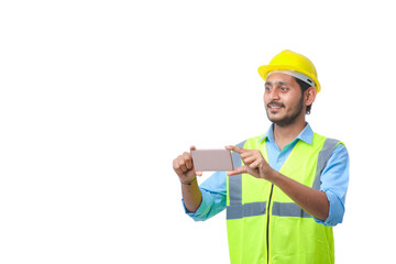 Young indian engineer wearing hardhat and using smartphone on white background.